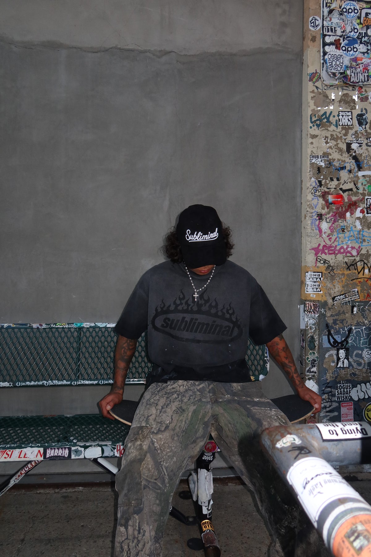Black Logo — Distressed Tee — Black, model seated on a bench with skateboard